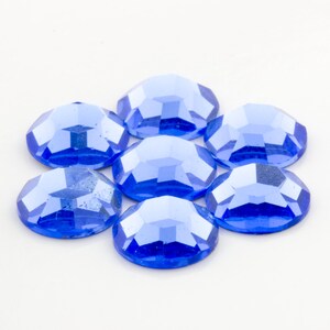 Op de afbeelding: Zeven blauwe glazen strassstenen in een cirkelvormige opstelling op een witte achtergrond.