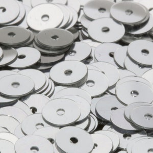 May include: A close-up shot of a pile of shiny, silver sequins. Each sequin is a flat, circular disc with a hole in the center. The sequins are scattered, creating a textured, reflective surface. Ideal for crafts and embellishments.