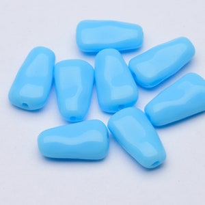 May include: Eight light blue, teardrop-shaped beads with a glossy finish. Each bead has a small hole at one end, suggesting they are for stringing. The beads are scattered on a white surface.