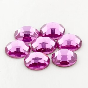 Op de afbeelding: Zeven roze, gefacetteerde, ovale strasssteentjes. De strasssteentjes hebben een glanzend, reflecterend oppervlak.