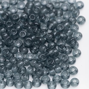 May include: A pile of small, round, grey glass beads. The beads are translucent and have a slightly iridescent sheen.