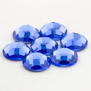 Op de afbeelding: Zeven blauwe, gefacetteerde, ronde strasssteentjes op een witte achtergrond.