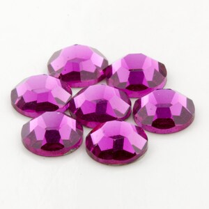 Op de afbeelding: Zeven ronde, gefacetteerde, roze strasssteentjes. De strasssteentjes hebben een glanzend, reflecterend oppervlak.
