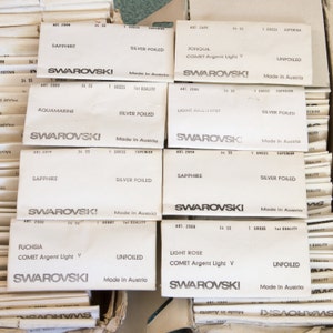 Puede incluir: Primer plano de varias cajas peque&ntilde;as blancas con el texto "SWAROVSKI" impreso en ellas. Cada caja tiene un nombre de color diferente y una descripci&oacute;n del producto, como "SAPPHIRE" o "LIGHT ROSE".