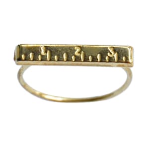 May include: A gold-toned ring with a ruler-shaped band. The band has markings for 1, 2, and 3 inches.