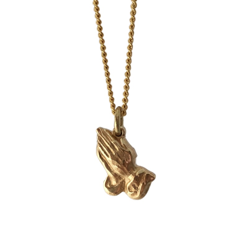 May include: A gold chain necklace with a small, detailed pendant of two hands clasped in prayer.