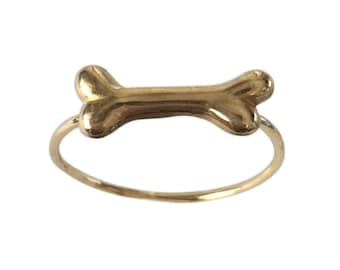 May include: A gold-colored ring with a bone-shaped design. The ring is thin and delicate.