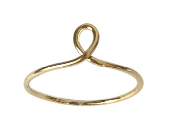 May include: A simple gold ring with a unique, twisted design. The ring is made of a thin wire and has a delicate, minimalist look.