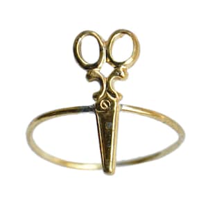 May include: A gold ring with a pair of scissors design. The ring is made of a thin band of metal and the scissors are detailed with a decorative design.