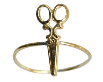 May include: A gold ring with a pair of scissors design. The ring is made of a thin band of metal and the scissors are detailed with a decorative design.