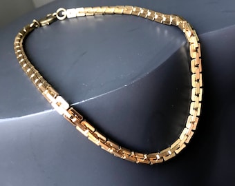 May include: A gold chain necklace with a box chain design. The chain is made of small, square-shaped links.