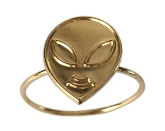 May include: A gold ring with an alien face design. The ring is simple and minimalist.