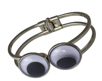 May include: A silver bangle bracelet with two large, white googly eyes. The eyes have black pupils.