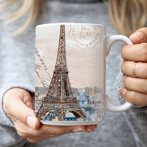 May include: White ceramic mug with a vintage postcard design featuring the Eiffel Tower in Paris, France. The postcard has a stamp that reads "10. 4. XI 1923 MONTMARTE".
