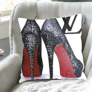 May include: A white cushion with a black and red illustration of two high-heeled shoes with a black and white LV logo in the background.