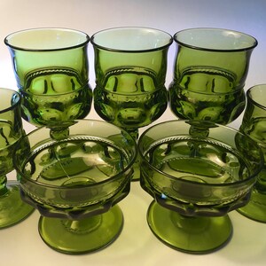 May include: A set of eight green glass goblets and dessert dishes. The goblets have a rounded bowl and a decorative stem. The dessert dishes have a shallow bowl and a similar base. The glassware is a vibrant green color.