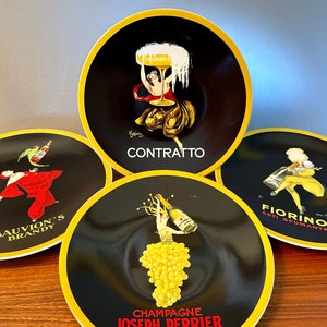 May include: Four black decorative plates with yellow rims. Each plate features a vintage advertisement design. One plate says "CONTRATTO", another "CHAMPAGNE JOSEPH PERRIER", a third "SAUVION'S BRANDY", and the last "FIORINO ASTI SPUMANTE".