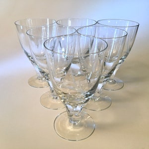 May include: Six clear stemmed glasses arranged in a triangular formation. Each glass has a wide bowl and a delicate etched design of leaves and stars. The glasses are made of clear glass and sit on a round base.