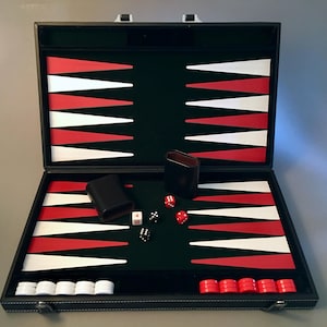 May include: A backgammon set in a black case with a dark green felt interior featuring red and white triangular points. The set includes two black dice cups, two black dice, two red dice, a white doubling cube, and white and red checkers.