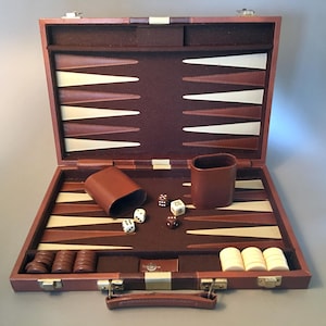 May include: Open backgammon set with a brown leather case, featuring a playing surface with alternating brown, beige, and white triangles. Includes dice, dice cups, and game pieces. The case is closed with metal clasps.