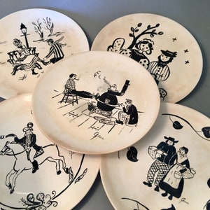 May include: A collection of five vintage ceramic plates with black and white illustrations. Each plate features a different scene, including people in winter attire, a man on a horse, and figures near a stove. The plates have a cream-colored background.