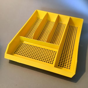May include: A bright yellow plastic utensil tray with four compartments and a perforated base. The tray is rectangular with slightly angled sides and is designed for organizing kitchen utensils. The overall dimensions are approximately 12 inches long by 9 inches wide.