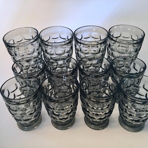 May include: A collection of clear, vintage drinking glasses. Each glass has a textured, honeycomb-like pattern and a short, rounded base. The glasses are arranged in neat rows, showcasing their design and clarity.