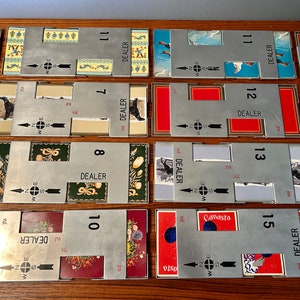 May include: A collection of vintage Canasta card game components. The set includes metal card holders with directional arrows and the word "DEALER." The cards feature floral and animal illustrations, with numbers 7, 8, 10, 11, 12, 13, and 15.