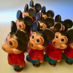 May include: A collection of vintage Mickey Mouse figurines. Each figurine has a black head with large ears, a red shirt, and blue pants. The toys are arranged in a triangular formation, showcasing their classic design.
