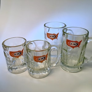 May include: Four clear glass mugs with handles. Each mug features the A&W logo, a map of the United States in orange and brown. The mugs vary in size and shape, with a textured exterior.