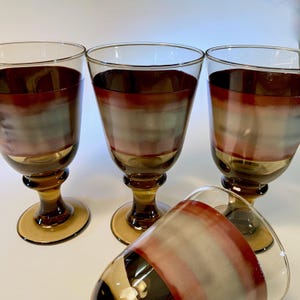 May include: Four vintage wine glasses with a unique design. The glasses feature a brown, red, and gray striped pattern on the bowl, with a brown stem and base. One glass is lying on its side, while the others stand upright.