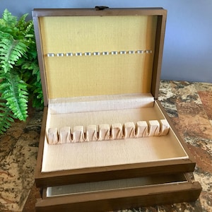May include: Open wooden silverware storage box with a light yellow interior and beige fabric lining. The box has slots for utensils and a pull-out drawer. The exterior is a dark brown color.
