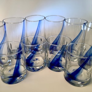 May include: A collection of clear glass tumblers and lowball glasses. Each glass features a vibrant blue swirl design. The glasses are arranged on a white surface, showcasing their elegant and artistic aesthetic. Ideal for serving beverages.