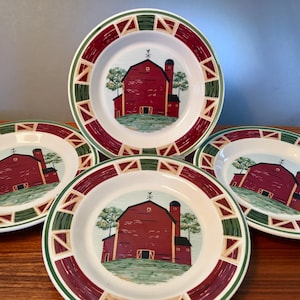 May include: Four white ceramic plates with a red barn scene in the center. The plates have a red and green border with a geometric design. The barn is red with a black silo and green grass.