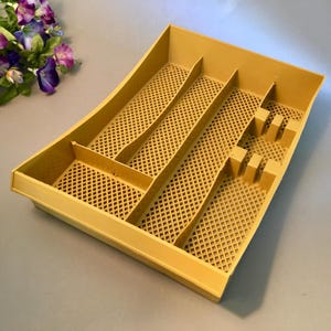 May include: A yellow plastic cutlery tray with multiple compartments and a lattice-style base. The tray is designed to organize silverware and utensils. The tray has a rectangular shape with curved sides and is made of durable plastic.