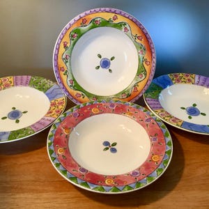 May include: Four white ceramic soup bowls with colorful floral and geometric designs. Each bowl has a different border pattern in shades of pink, green, yellow, and purple. The center of each bowl features a small blue floral design.