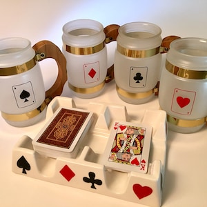 May include: Four frosted glass beer steins with wooden handles and gold accents, each displaying a playing card suit. A white ceramic ashtray with playing card suit symbols and a deck of cards are also present.
