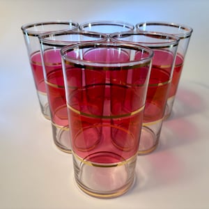 May include: Set of six vintage highball glasses. Each glass features a clear base, a vibrant red center section, and gold bands. The rims are also trimmed with gold. These glasses are perfect for serving cocktails or other beverages.