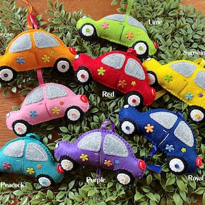 May include: Nine felt car ornaments in various colors, including red, yellow, blue, green, purple, pink, and orange. Each car has a different name written on it, such as "Mac n Cheese", "Sunshine", "Lime", "Peacock", and "Royal".