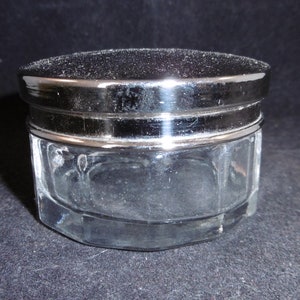 Könnte beinhalten: Ein kleines, klares Glasgefäß mit einem silbernen Deckel. Das Gefäß hat eine sechseckige Form und ist perfekt zum Aufbewahren von kleinen Gegenständen.