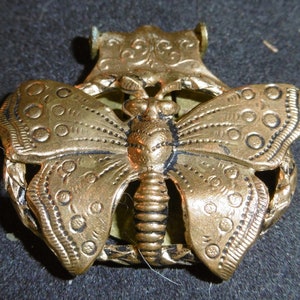 May include: A gold-toned metal butterfly brooch with intricate details and a textured surface.