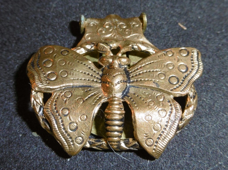 May include: A gold-toned metal butterfly brooch with intricate details and a textured surface.