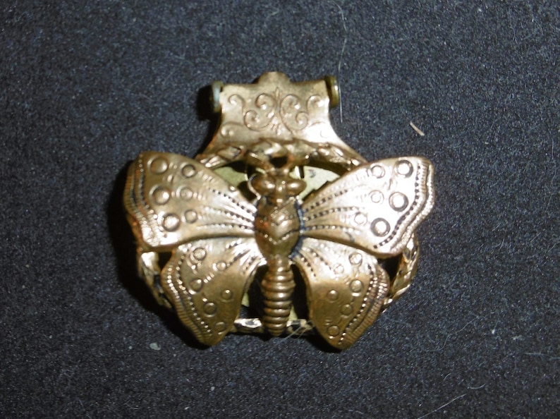 May include: Gold-toned metal butterfly charm with intricate details. The butterfly has a detailed body and wings with a decorative border.