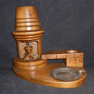May include: A wooden fireplace-shaped ashtray with a metal ashtray insert. The fireplace has a carved wooden chimney and a small wooden bucket hanging inside.