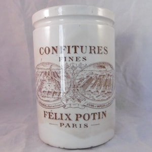 May include: White ceramic jar with brown lettering that reads "Confitures Fines Felix Potin Paris" and a brown illustration of a factory.