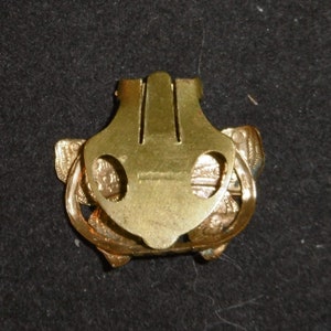 May include: Gold-toned metal clasp with a decorative butterfly design. The clasp has two loops on either side and a central bar with three vertical ridges.