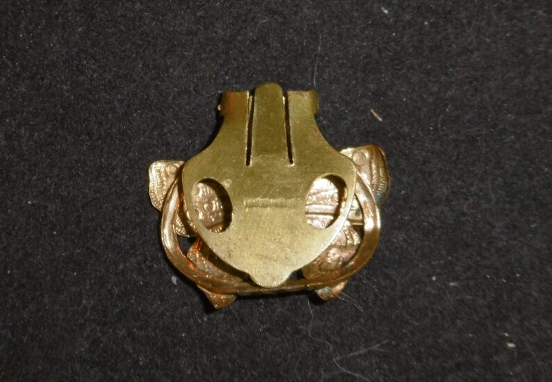 May include: Gold-toned metal clasp with a decorative butterfly design. The clasp has two loops on either side and a central bar with three vertical ridges.