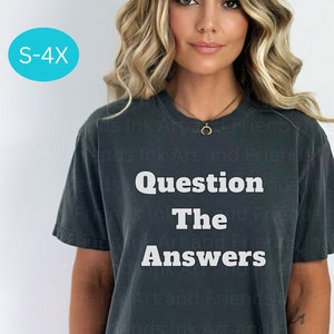 May include: Dark gray t-shirt with the text "Question The Answers" in white block letters. The shirt has short sleeves and a relaxed fit. A size range of S-4X is indicated in a light blue circle.