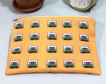 May include: A yellow zippered pouch with a repeating pattern of cassette tapes. The pouch is lying flat on a white surface.