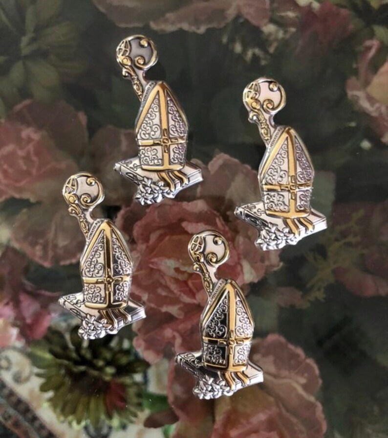 May include: Four silver and gold-toned metal charms shaped like a small building with a pointed roof and a small orb on top. The charms have intricate details and are set against a background of pink and green roses.